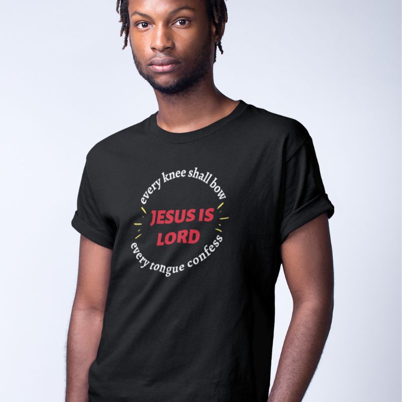 Black man wearing black Christian unisex T-shirt that says in a circle "Every knee shall bow, every tongue confess" with "Jesus is Lord" in the middle