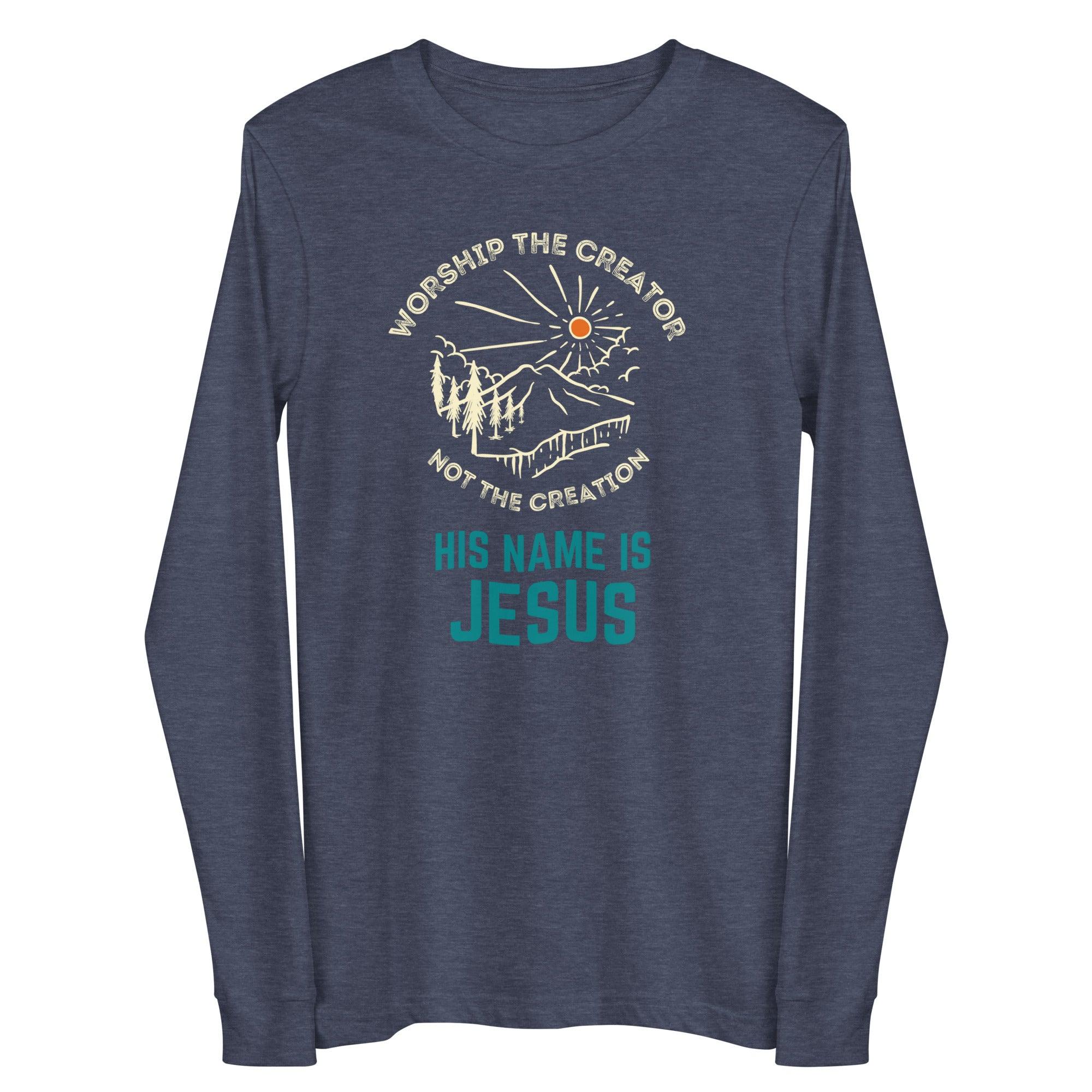 Flatlay of a blue long sleeve Christian shirt. There is a graphic of a mountain, trees, and sun. Over the graphic, it says "Worship the creator", and under it says "not the creation". On the bottom, it says "His name is Jesus". This shirt is sold at Amela&