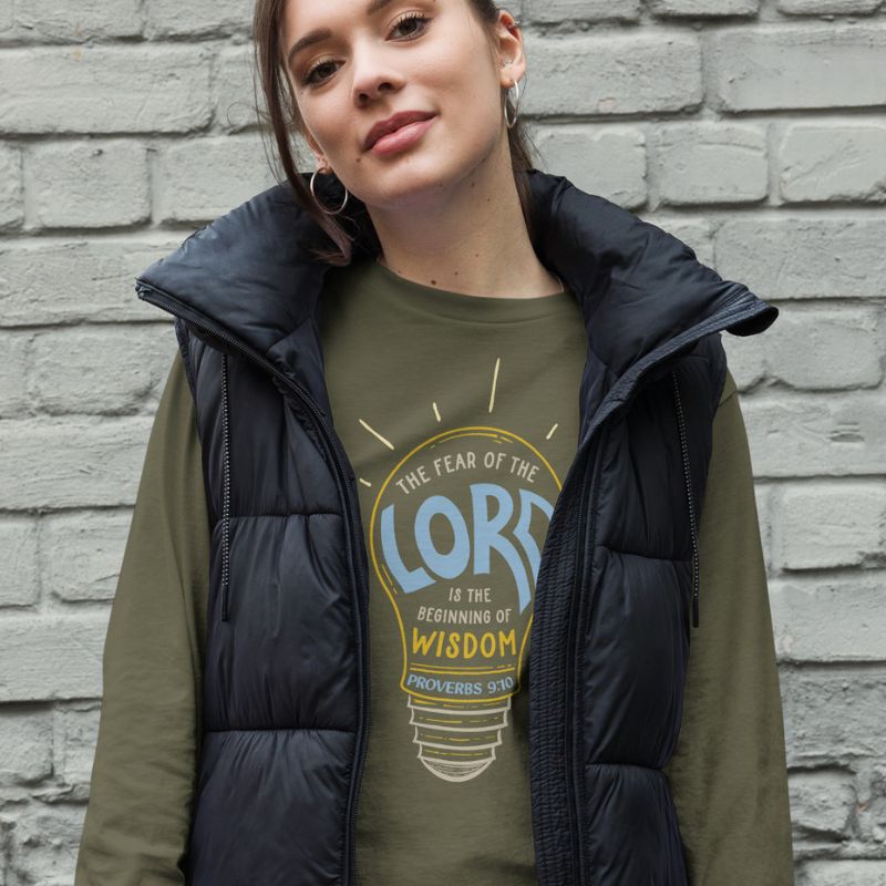 White woman wearing a green Christian long-sleeve shirt. The design is a lightbulb, with text inside, that says, &quot;The fear of the Lord is the beginning of wisdom - Proverbs 9:10&quot;