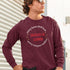 White man wearing maroon Christian unisex long sleeve shirt that says in a circle "Every knee shall bow, every tongue confess" with "Jesus is Lord" in the middle